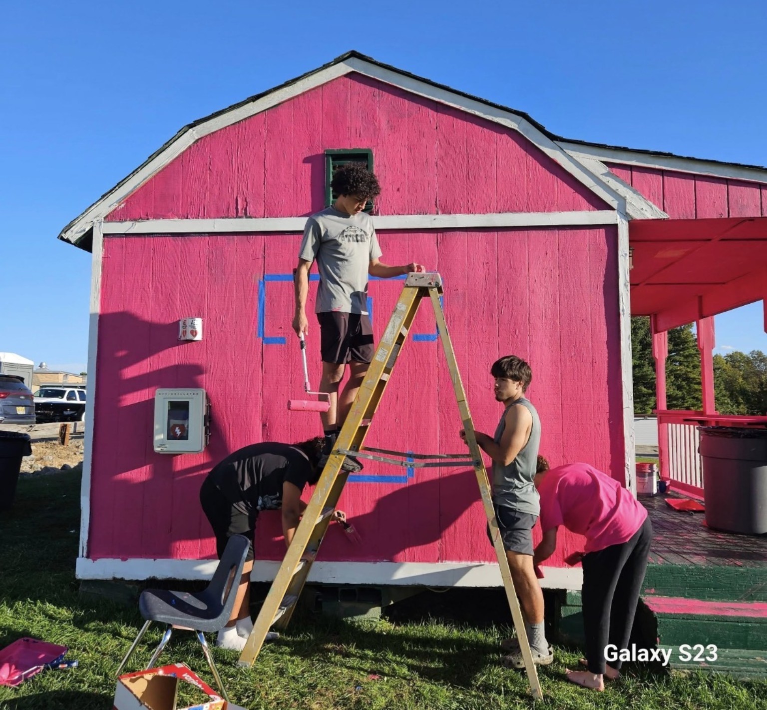 Players painting the building magenta using rollers and a ladder